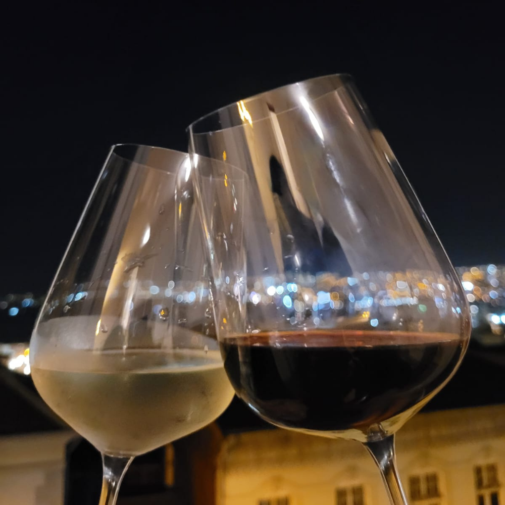 Brindis nocturno con copas de vino tinto y blanco, con el fondo iluminado de la ciudad de Valparaíso.