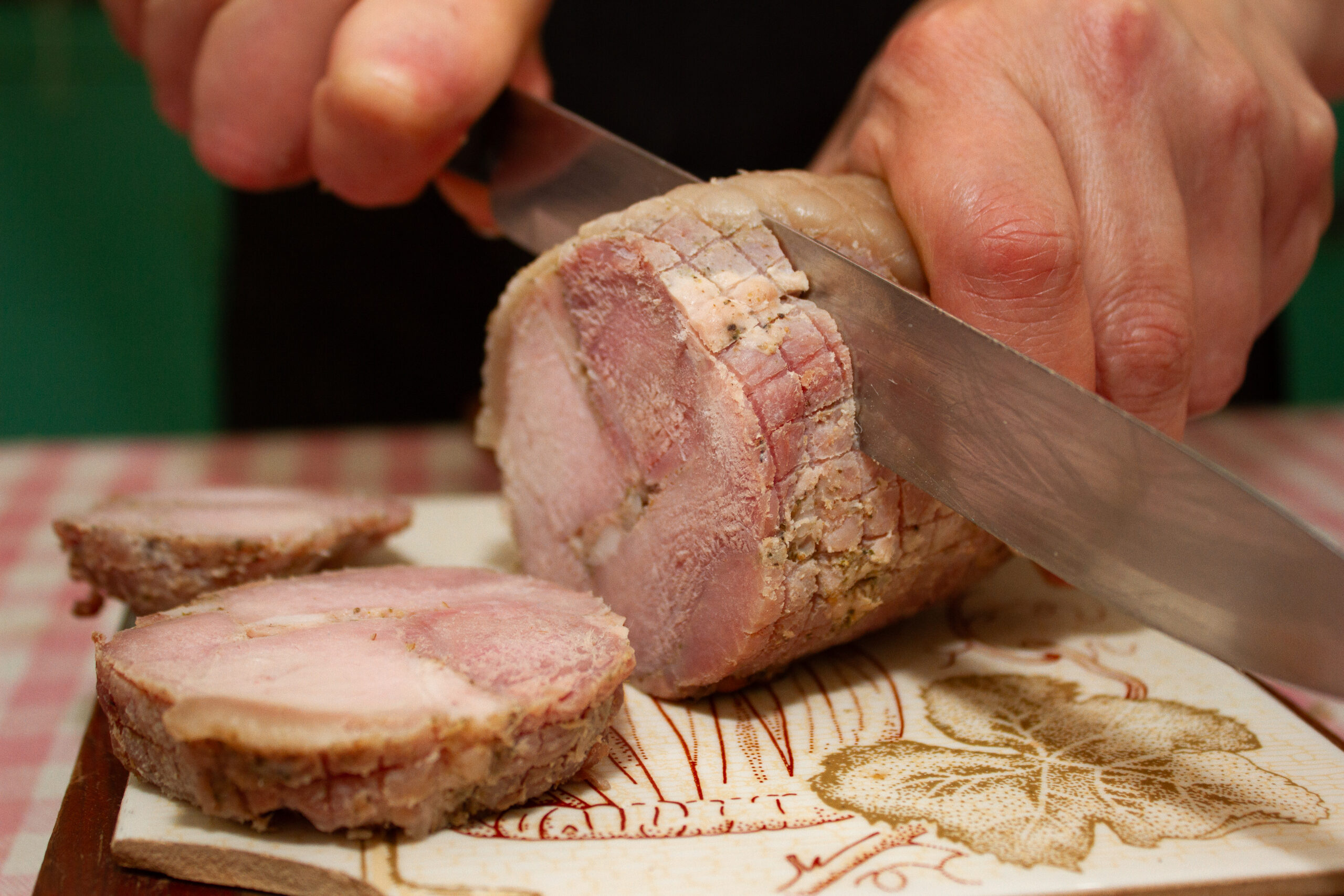 Mano sosteniendo una cuchara mientras se vierte una salsa cremosa de matico desde una jarra blanca sobre un plato de machas frescas, decoradas con cilantro y finas hierbas. La imagen captura el momento preciso en que la salsa cae suavemente, resaltando la textura y el color del plato en una presentación elegante y tradicional.